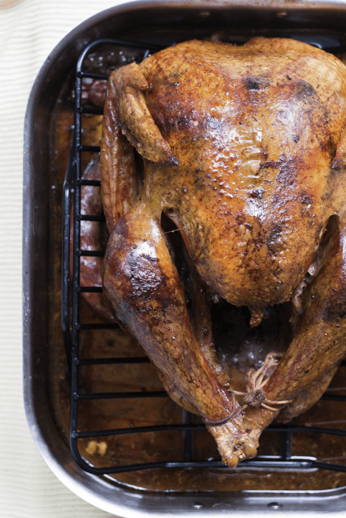 A golden-brown rotisserie chicken with a side of fresh herbs, showcasing a perfectly cooked meal for various recipes.